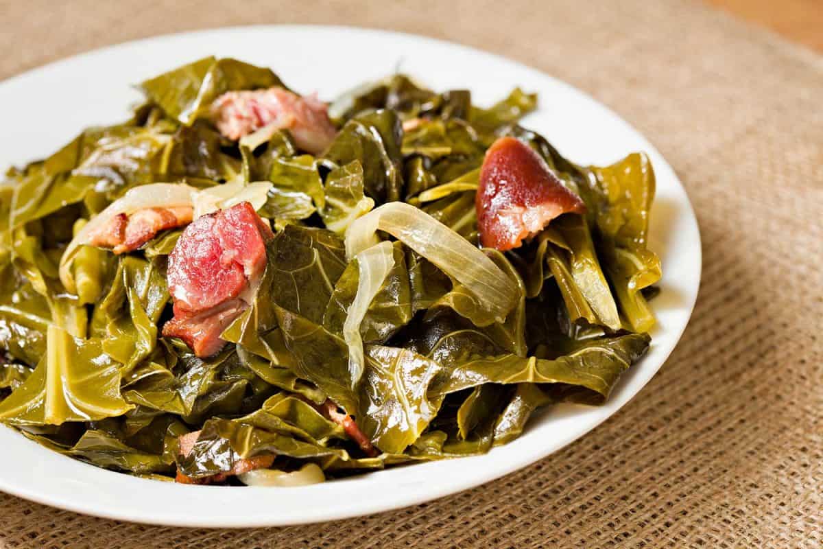 A high angle close up shot of a white bowl full of collard greens and ham hock pieces
