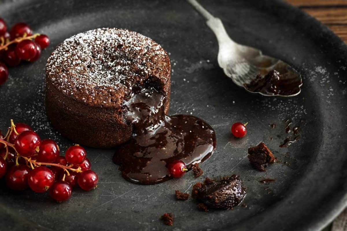 A single serving of warm chocolate lava cake sprinkled with powdered sugar with a bite taken out. 