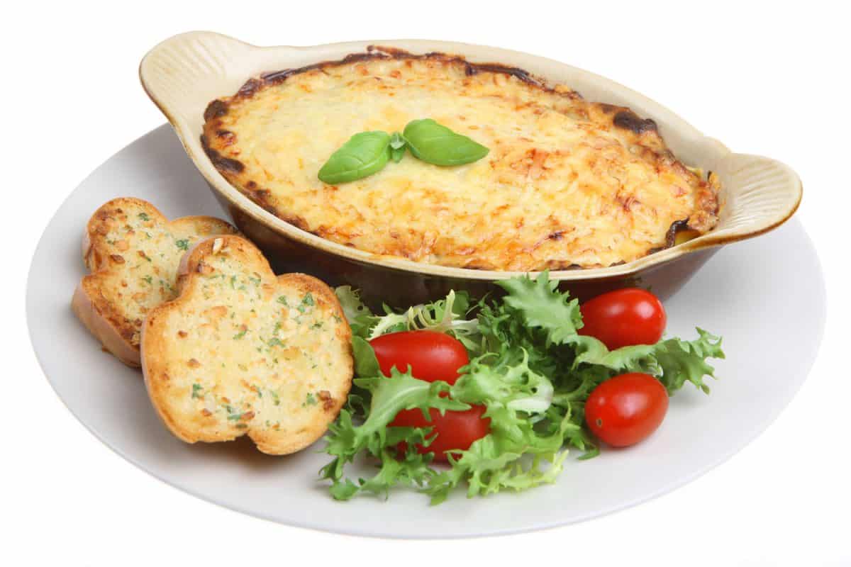 A small lasagna with crispy bread on the side and leafy greens