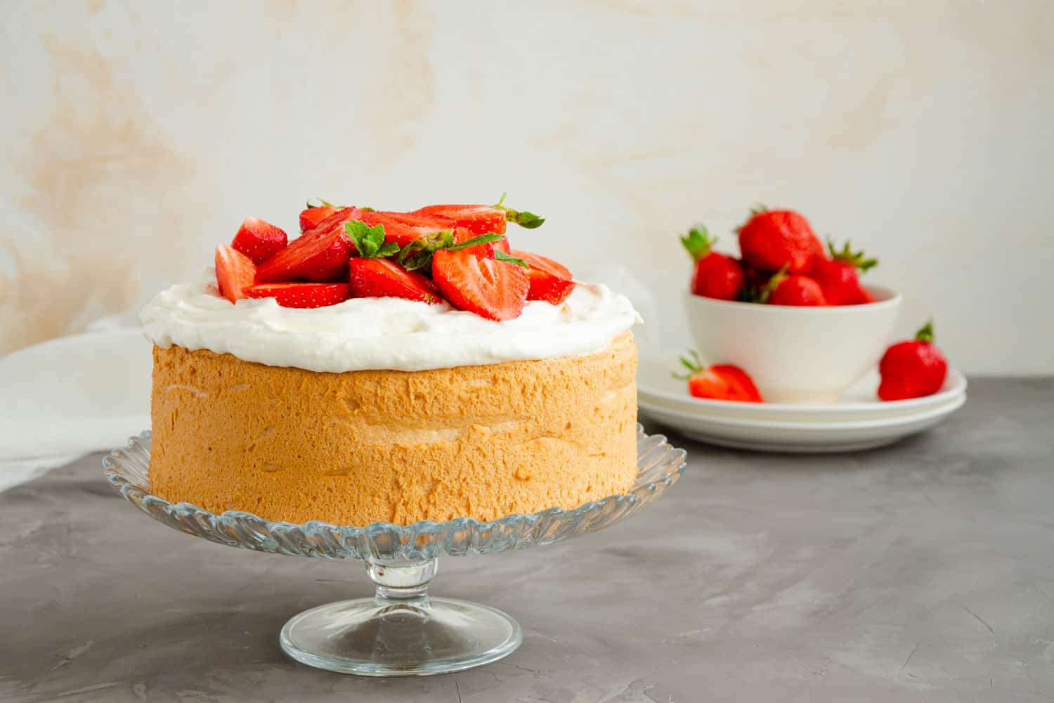 Angel food cake with whipped cream and slices of fresh strawberries on top on a concrete background