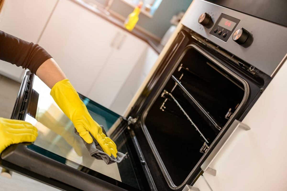 Close up on woman's hands in yellow protective rubber gloves cleaning oven with rag