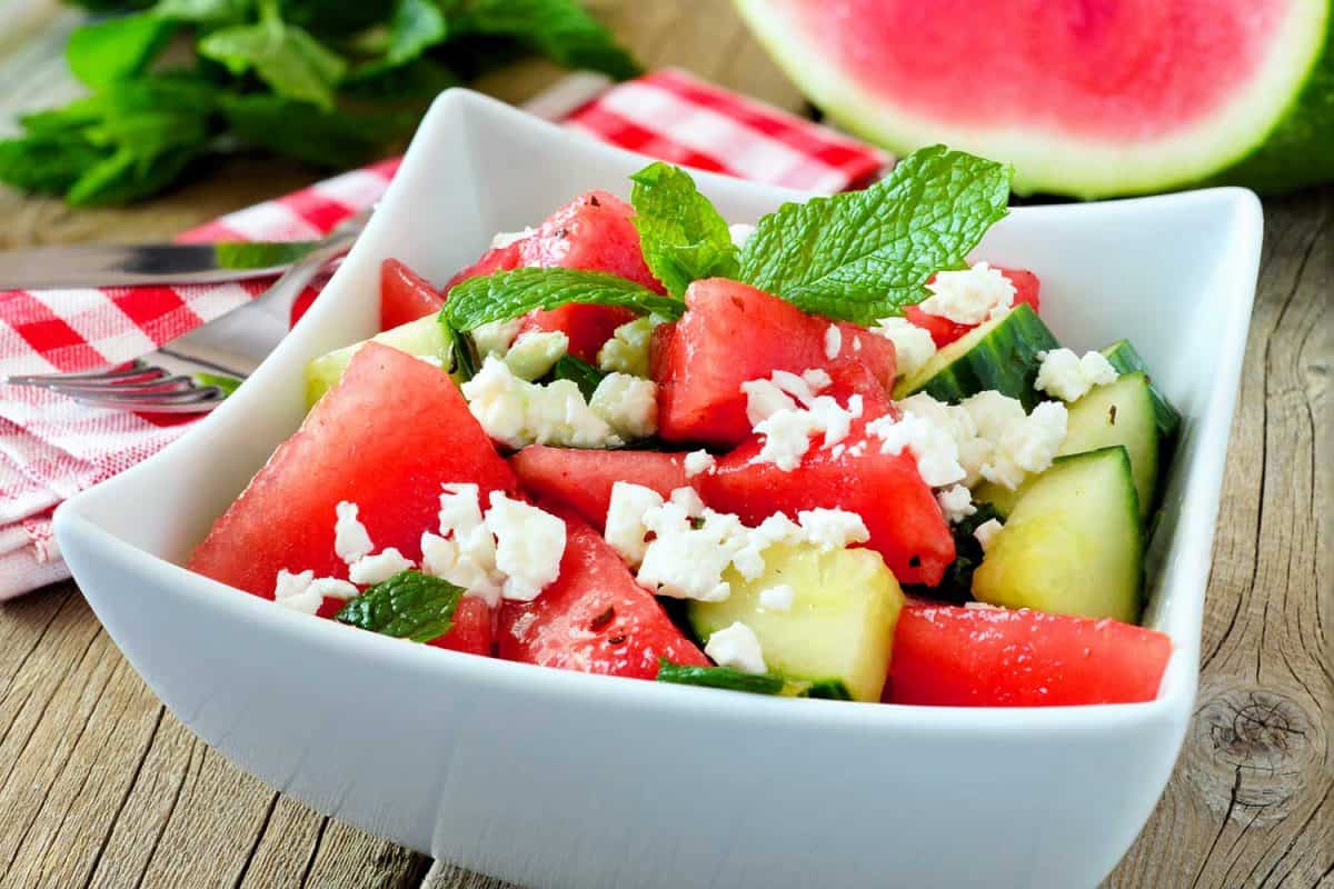 Delicious watermelon, cucumber and feta cheese salad in square bowl on wood background