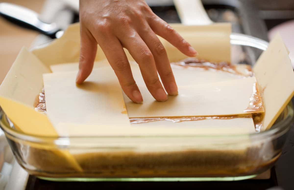 Female hand arranges sheets of lasagne pasta in preparation for the oven.