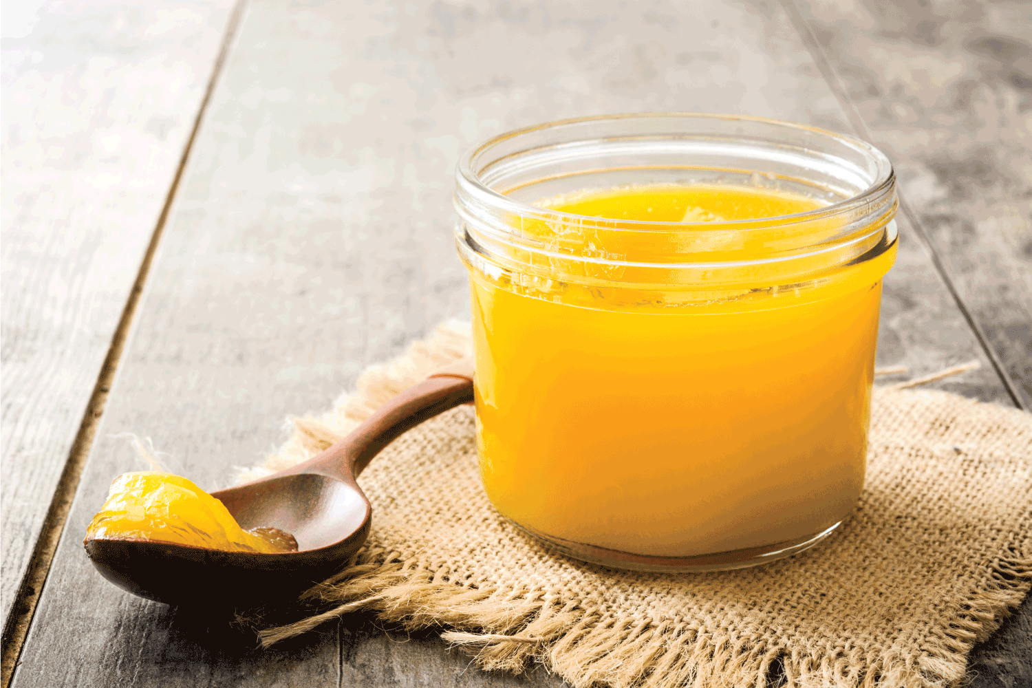 Ghee or clarified butter in jar and wooden spoon on wooden table