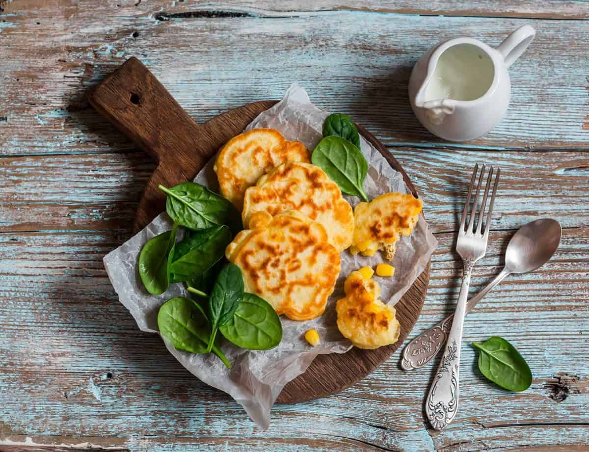Gluten free corn fritters and fresh spinach on a wooden board