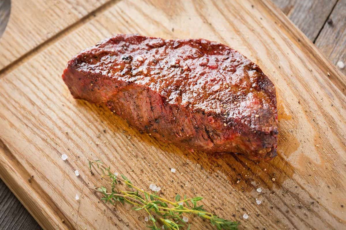 Hot grilled whole Denver steak on wooden board with herbs