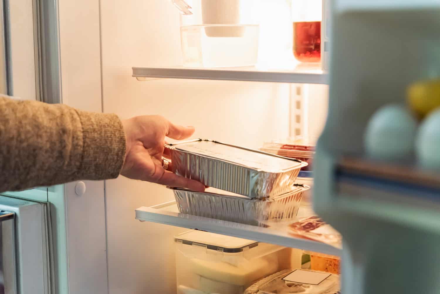 Man's hand taking takeout meal out of refrigerator. Horizontal indoors close-up with copy space.