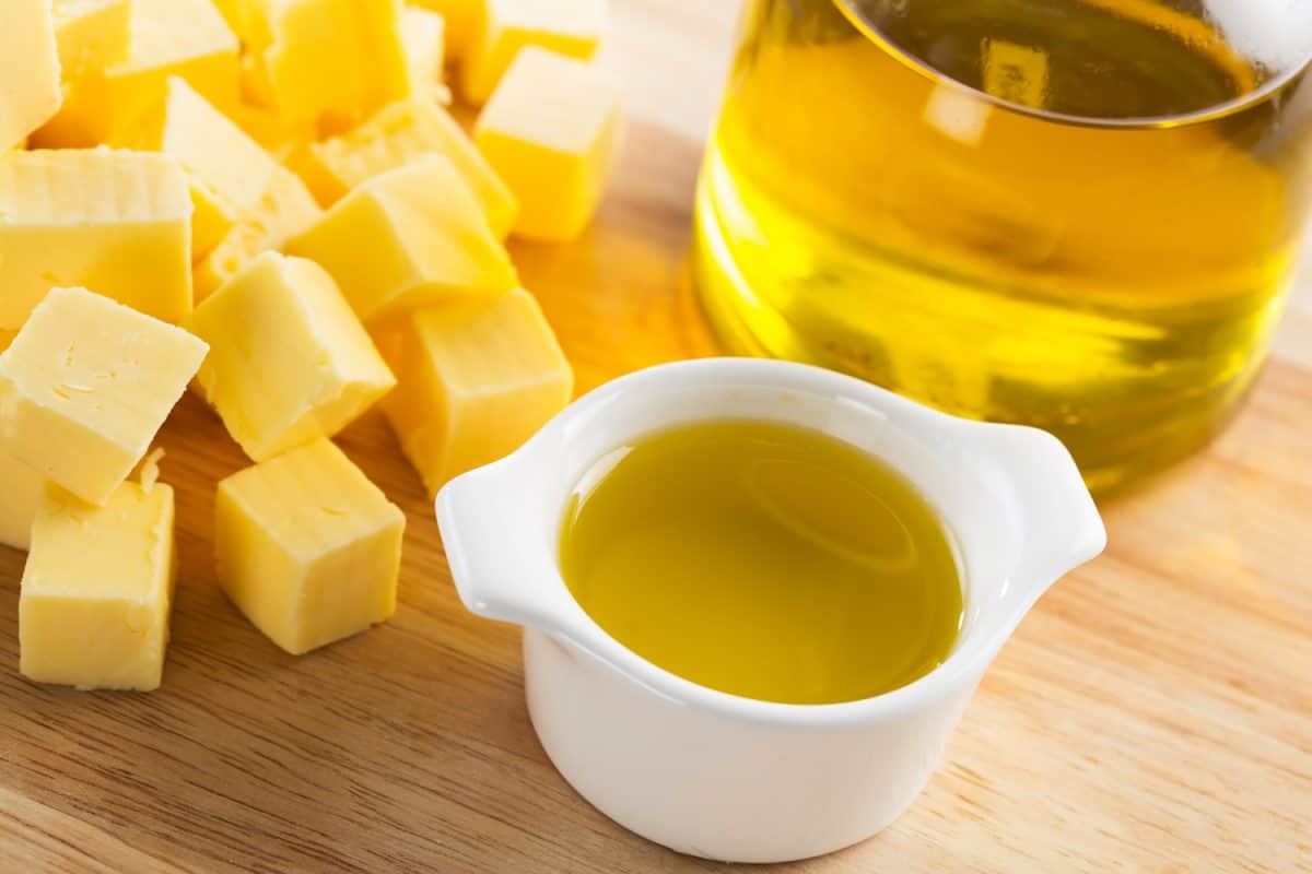 Olive oil in small glass container with bottle of oil and cubes of butter
