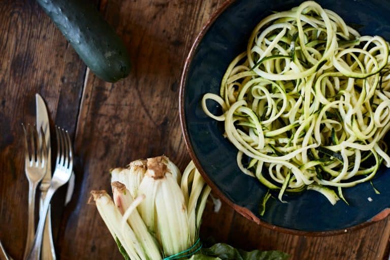 Perfectly sliced Zucchini noodles on a small bowl with forks and a break knife on the table, How Long Do You Cook Zucchini Noodles?