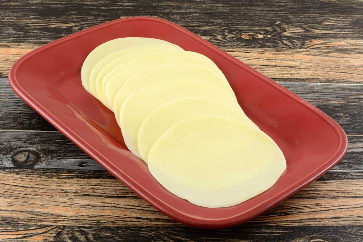 Provolone cold cut cheese slices on red serving platter on table