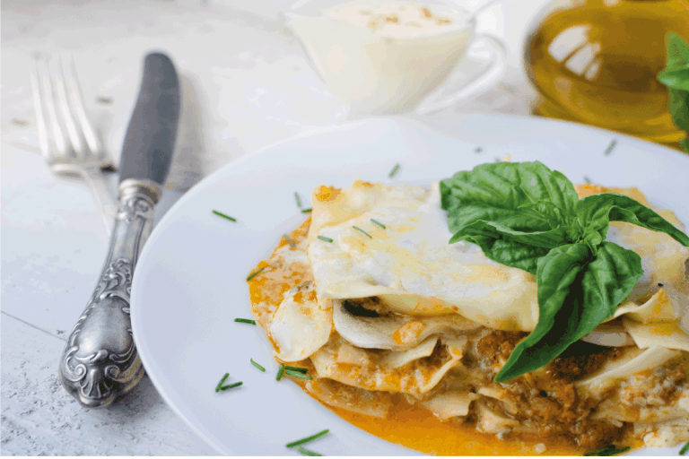 Traditional lasagna made with minced beef bolognese sauce and bechamel sauce topped with basil leaves. Portion of tasty homemade lasagna on white wooden table. Does Lasagna Finish With Pasta Or Sauce