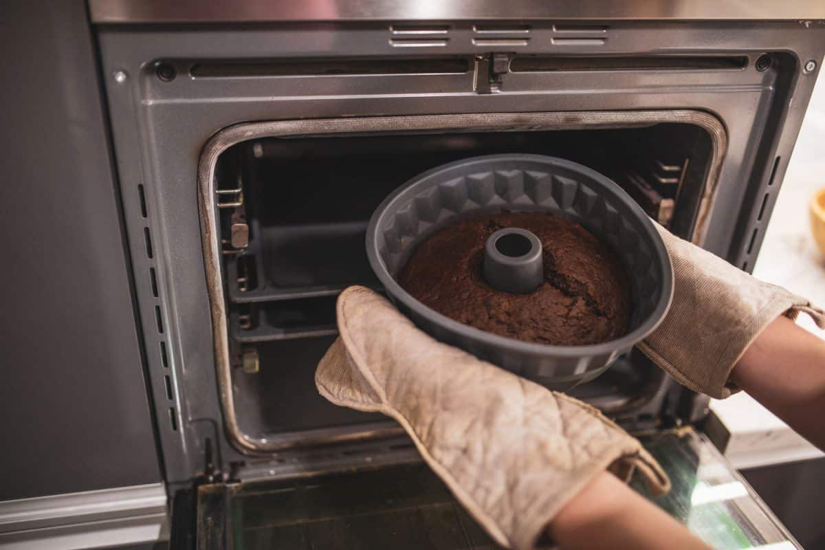 Unrecognizable woman in oven mitts, taking a bundt cake in a silicone tray out of the oven