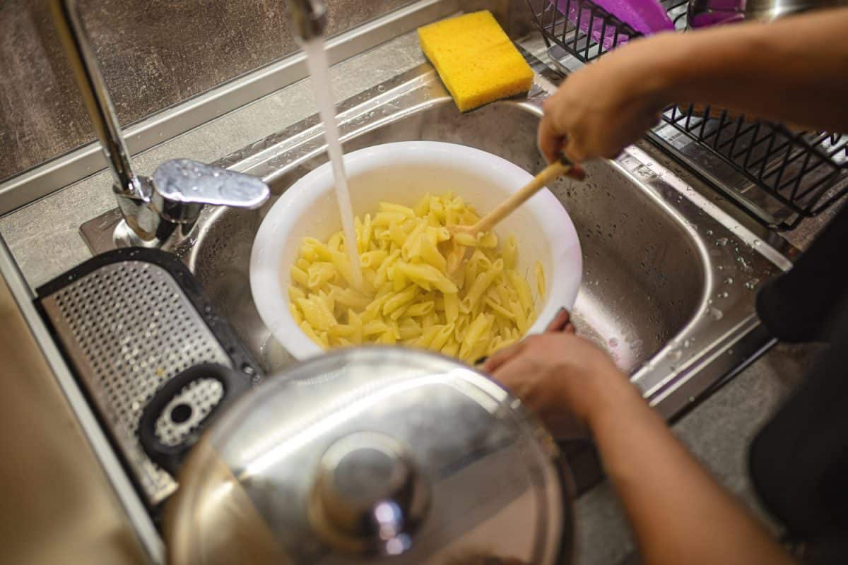 Woman washing pasta in a sink before cooking it.