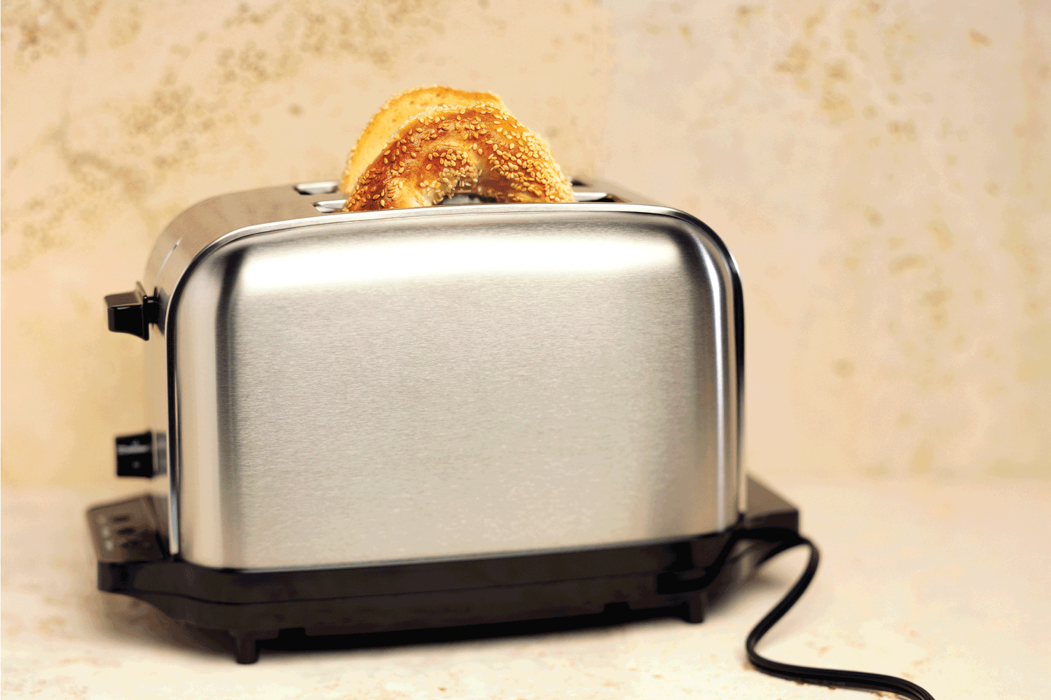 bagel with sesame seeds popping out of stainless steel toaster