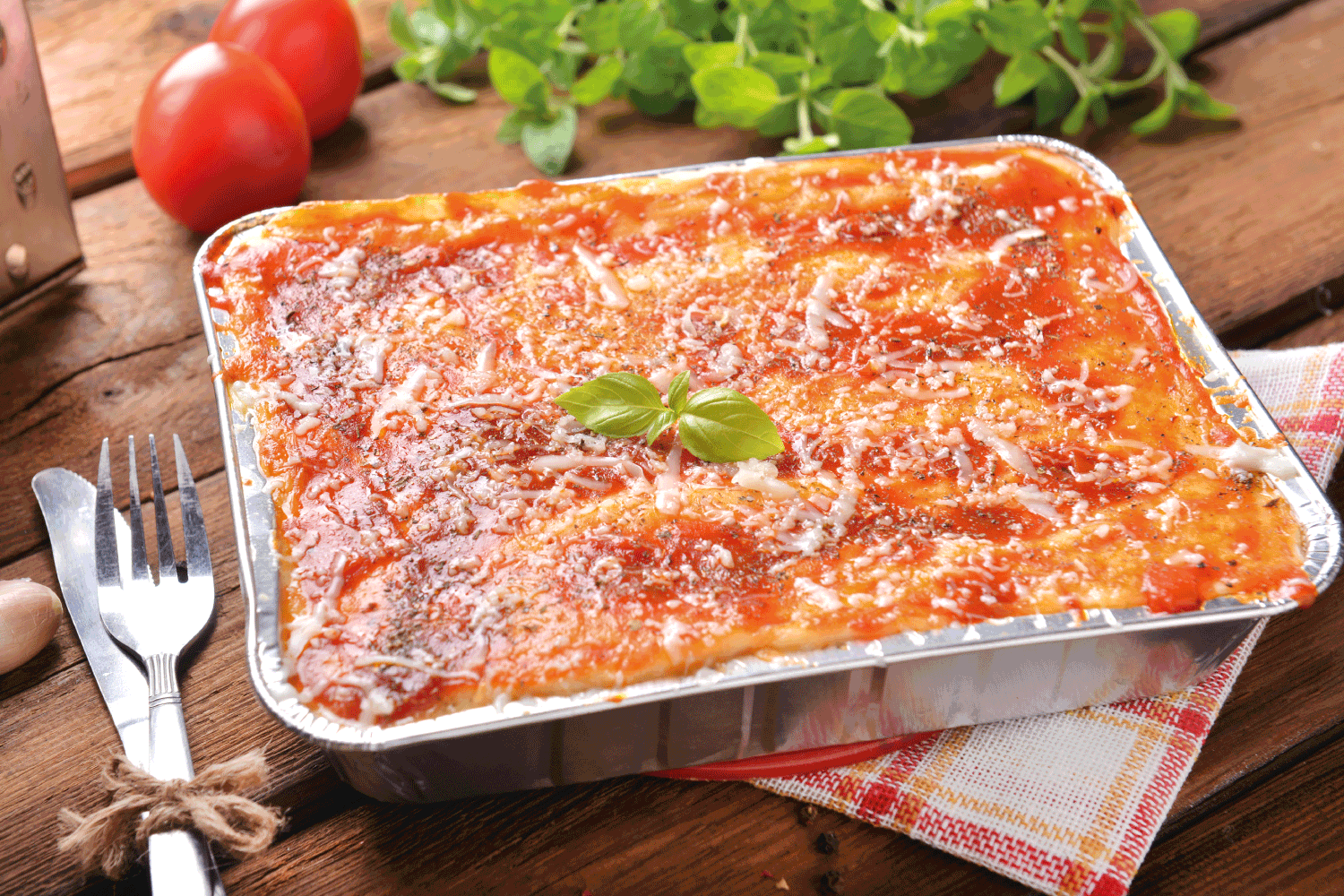bolognese lasagna in a aluminum tray with cutlery on the side