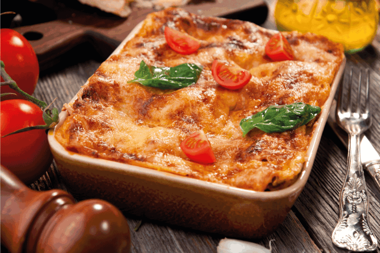 lasagna in a ceramic baking dish with cherry tomatoes on top of wooden table. Should You Defrost a Lasagna Before Cooking it