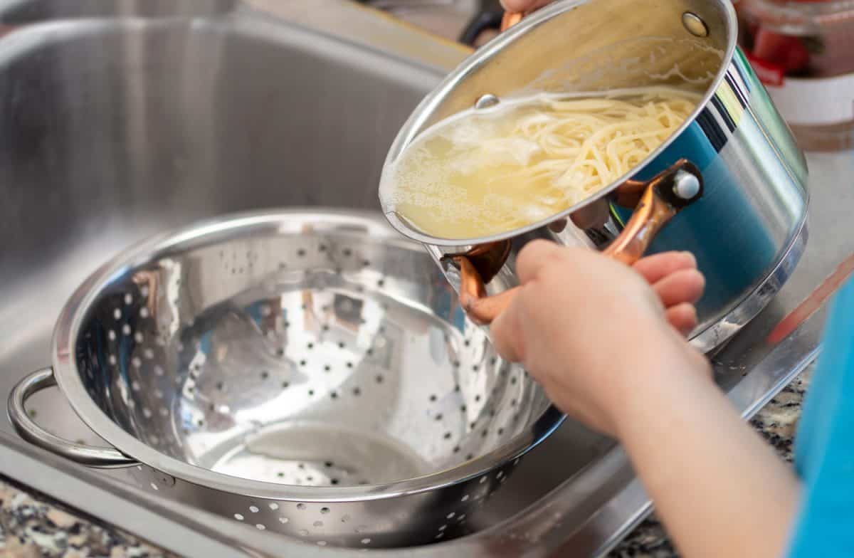 woman separating water from spaghetti withempty silver colander
