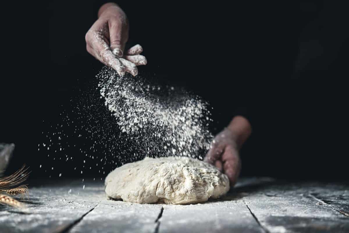 A Chef spraying flour on a dough