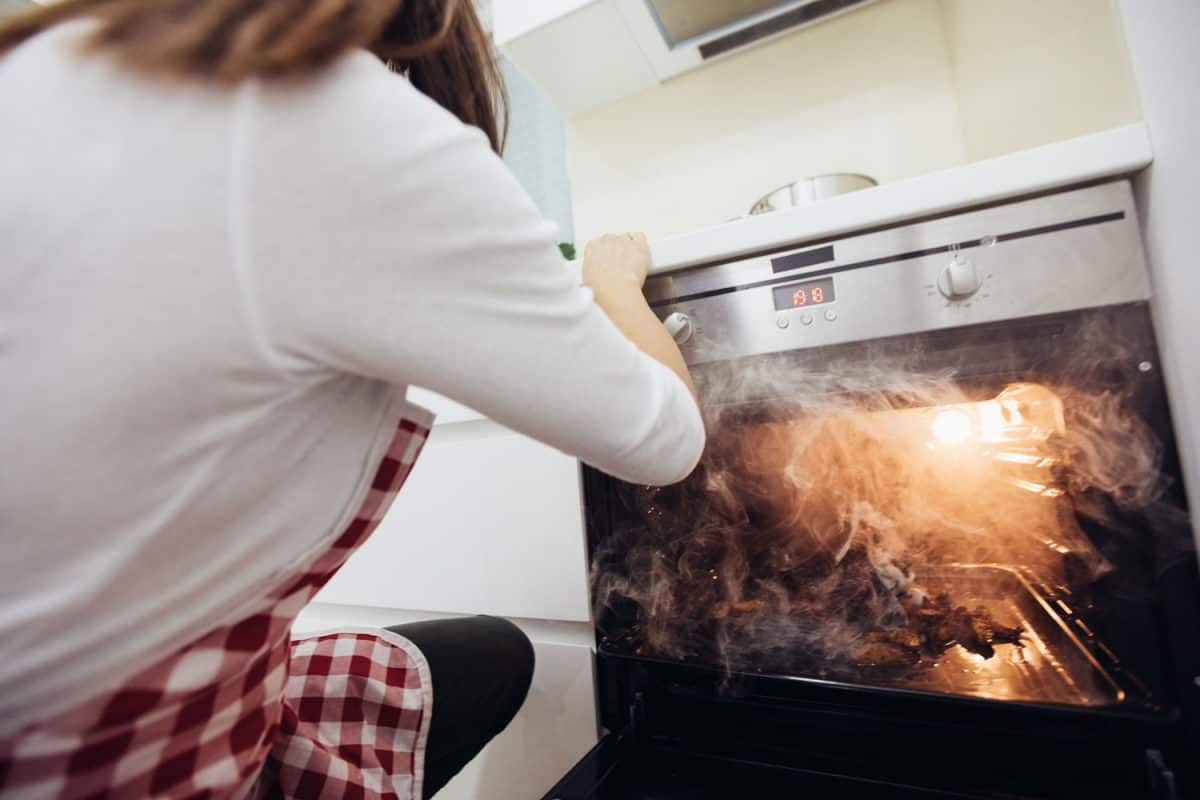 A woman checking the oven due to smoking beef