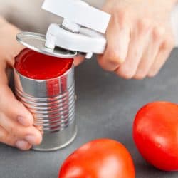 A woman is carefully opening a can of tomato paste on a kitchen counter using a white plastic can opener, How To Use A Pampered Chef Can Opener