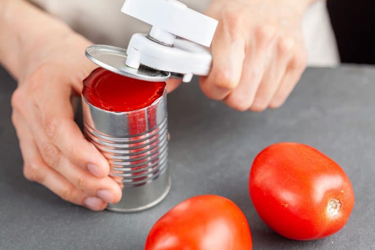 A woman is carefully opening a can of tomato paste on a kitchen counter using a white plastic can opener, How To Use A Pampered Chef Can Opener