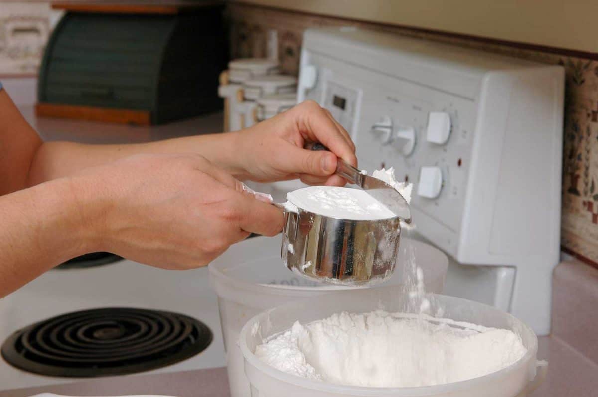 A woman measures a cup of flour for baking