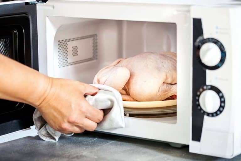 A woman microwaving a whole dressed chicken in the microwave, Does Microwaving Chicken Make It Rubbery?