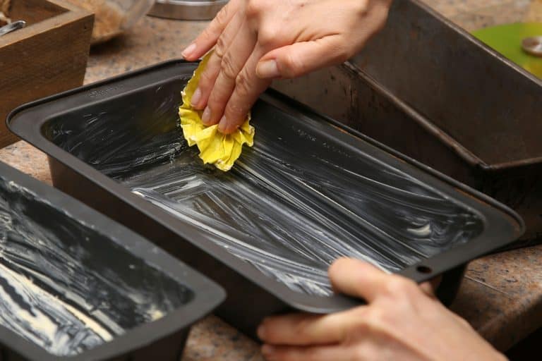 A woman smearing butter onto a baking pan before putting dough in, How To Easily And Thoroughly Flour A Pan
