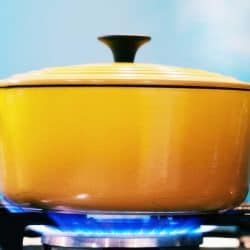 A yellow enamel casserole with its lid on, sits on a lit gas burner creating steam as it heats, Can Le Creuset Ceramic Go On The Stove?
