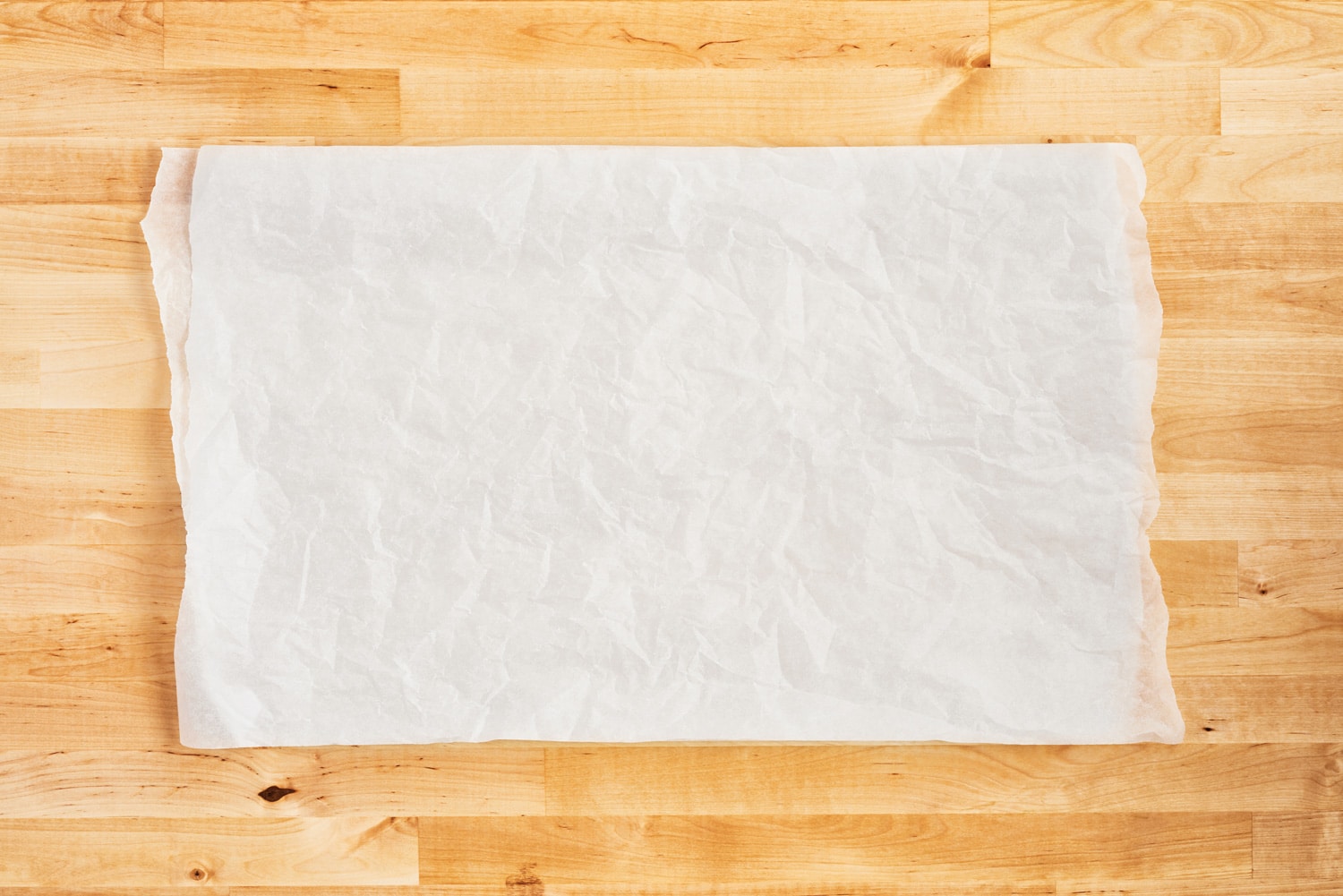 Crumpled piece of white parchment or baking paper on wooden table. Top view. Copy space for text and design element.