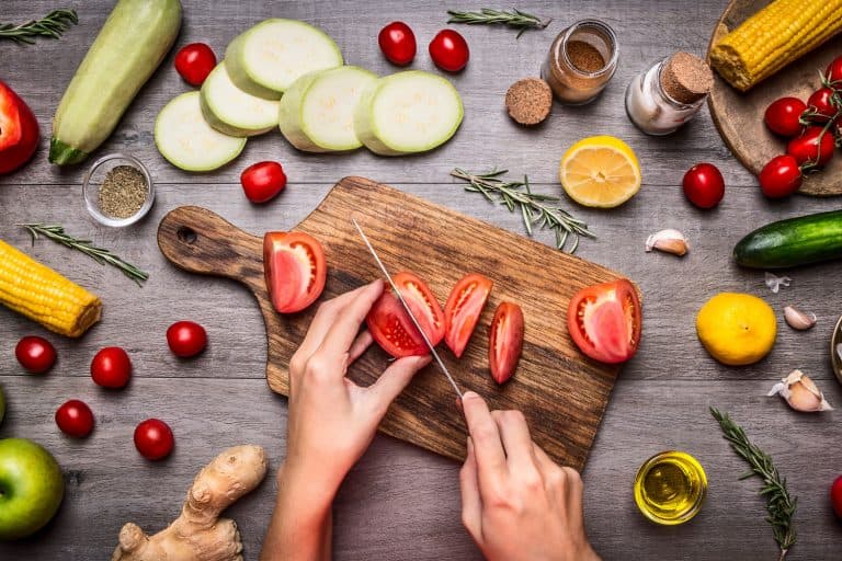 Female hand cut tomatoes on rustic kitchen table, around lie ingredients, vegetables, fruits, and spices, Healthy foods, cooking and vegetarian concept, What Is The Best Knife For Cutting Tomatoes?