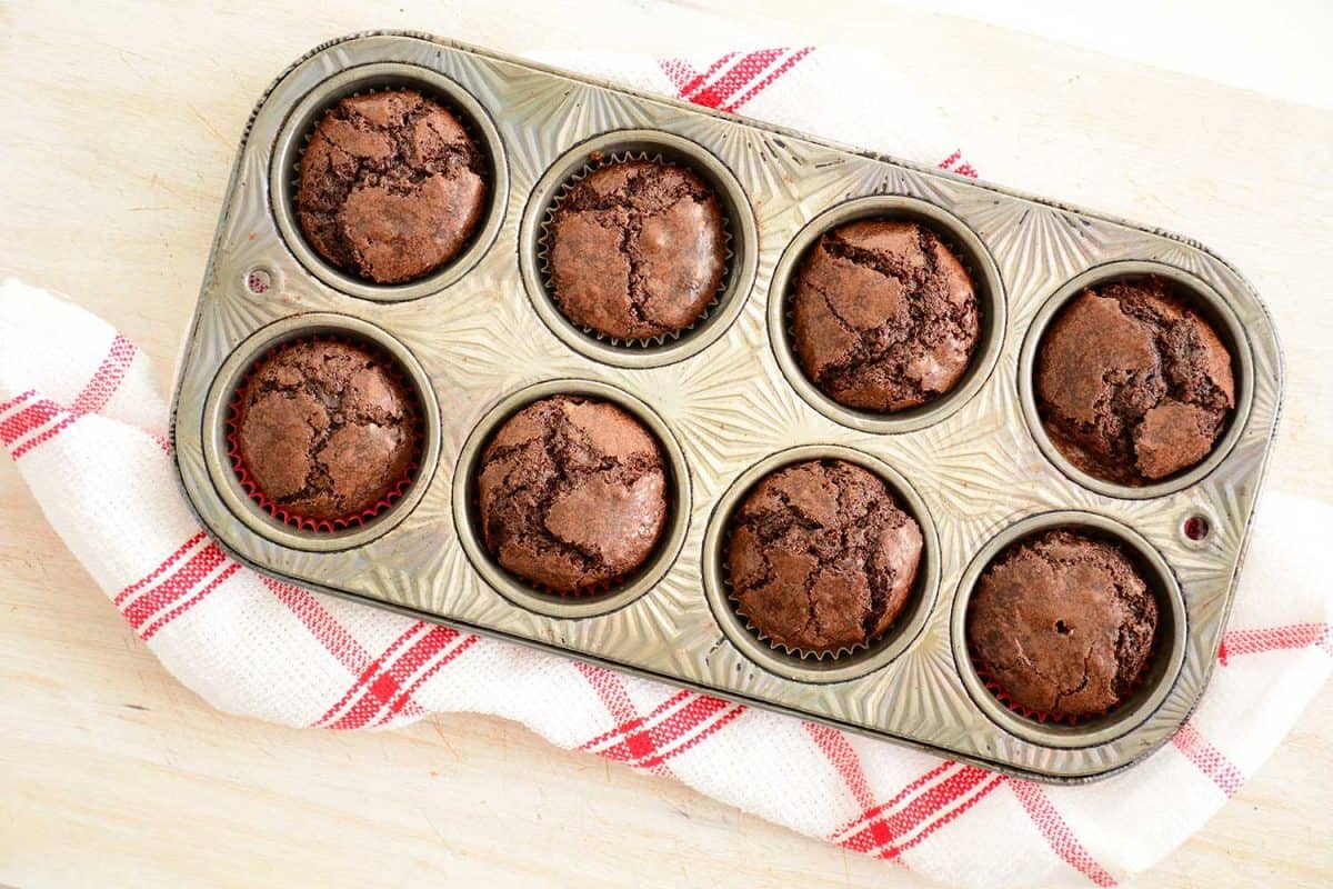 Fresh baked mini chocolate brownies in vintage muffin tin on red and white tea towel in flat lay composition