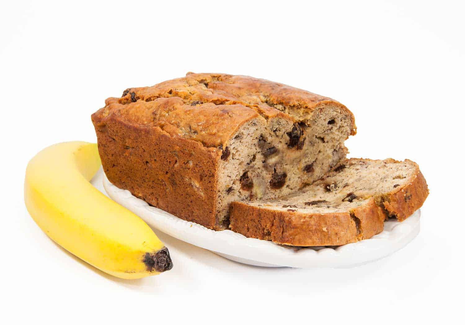 Homemade banana bread with raisins on a white dish with a banana against a white background