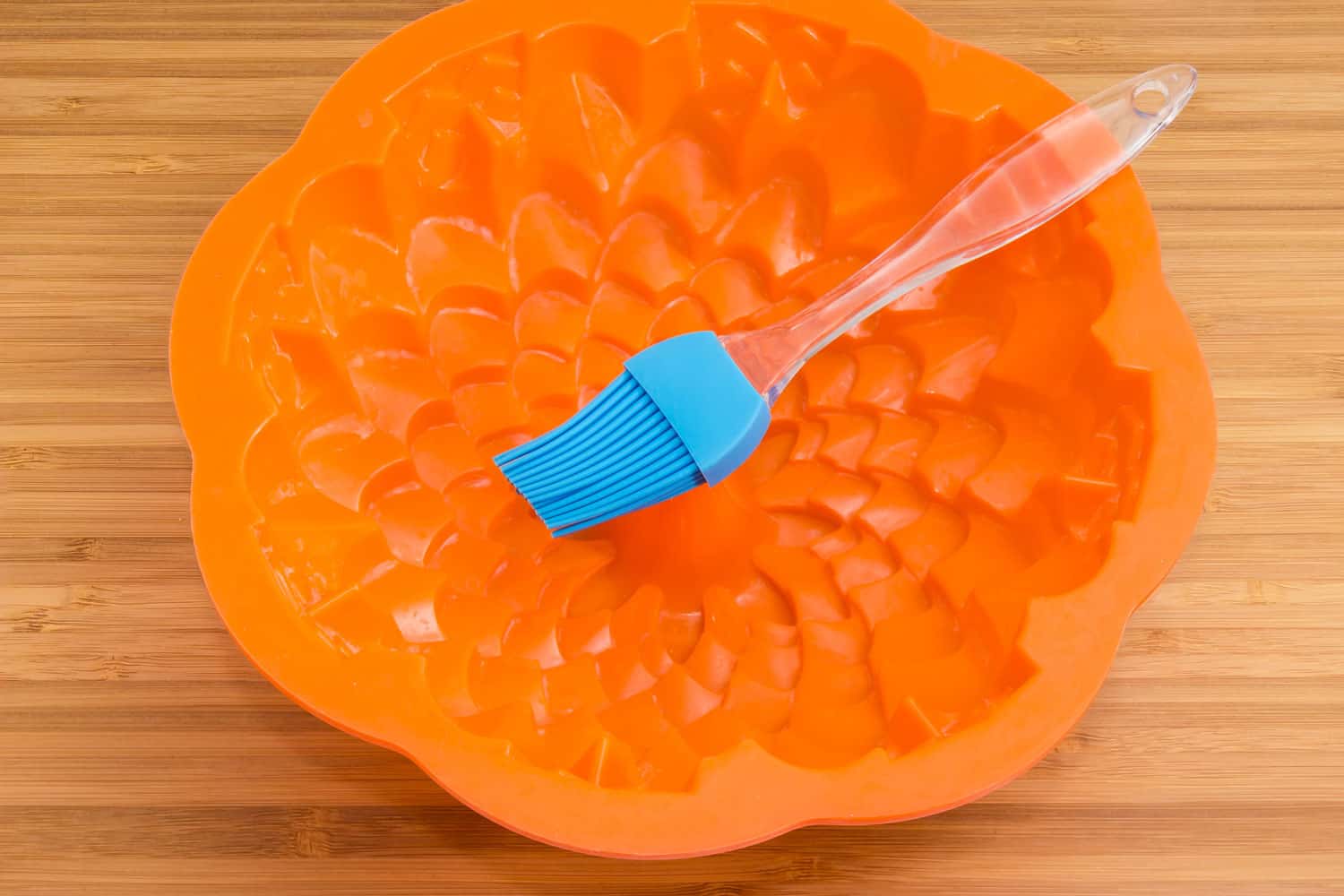 Modern silicone pastry brush in empty silicone cake pan in bundt-style on a wooden bamboo cutting board