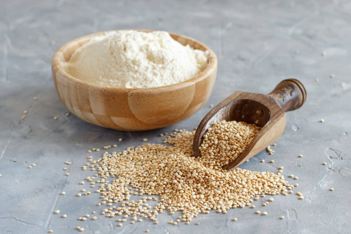 Raw dry white quinoa flour seeds in a wooden bowl and a wooden scoop