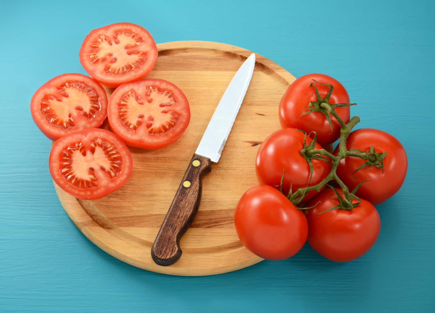Ripe tomatoes, whole and sliced with serrated knife on wooden cutting board