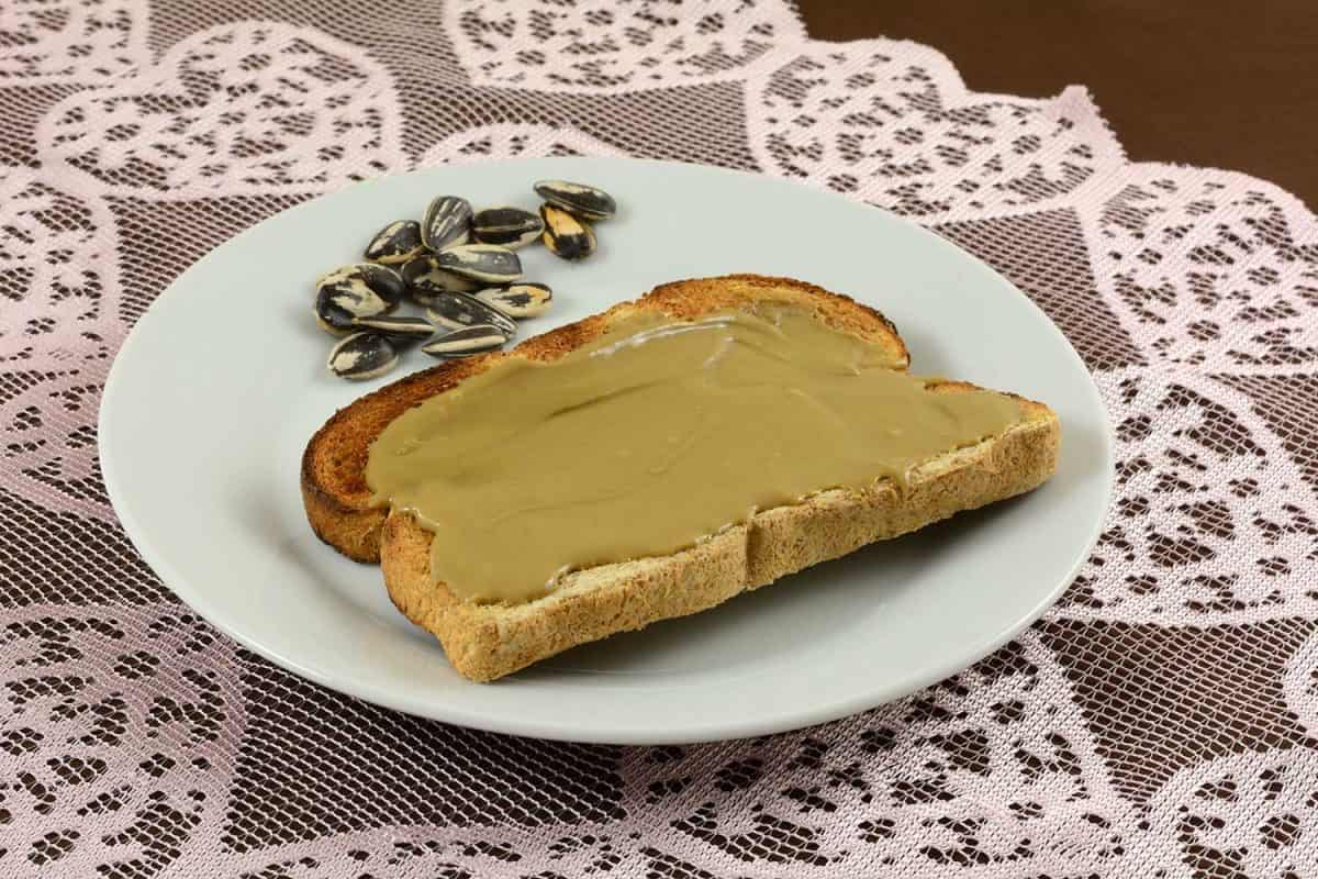 Sunflower butter on whole wheat toasted bread with sunflower seeds on white plate withe sunflower seeds on lace table runner