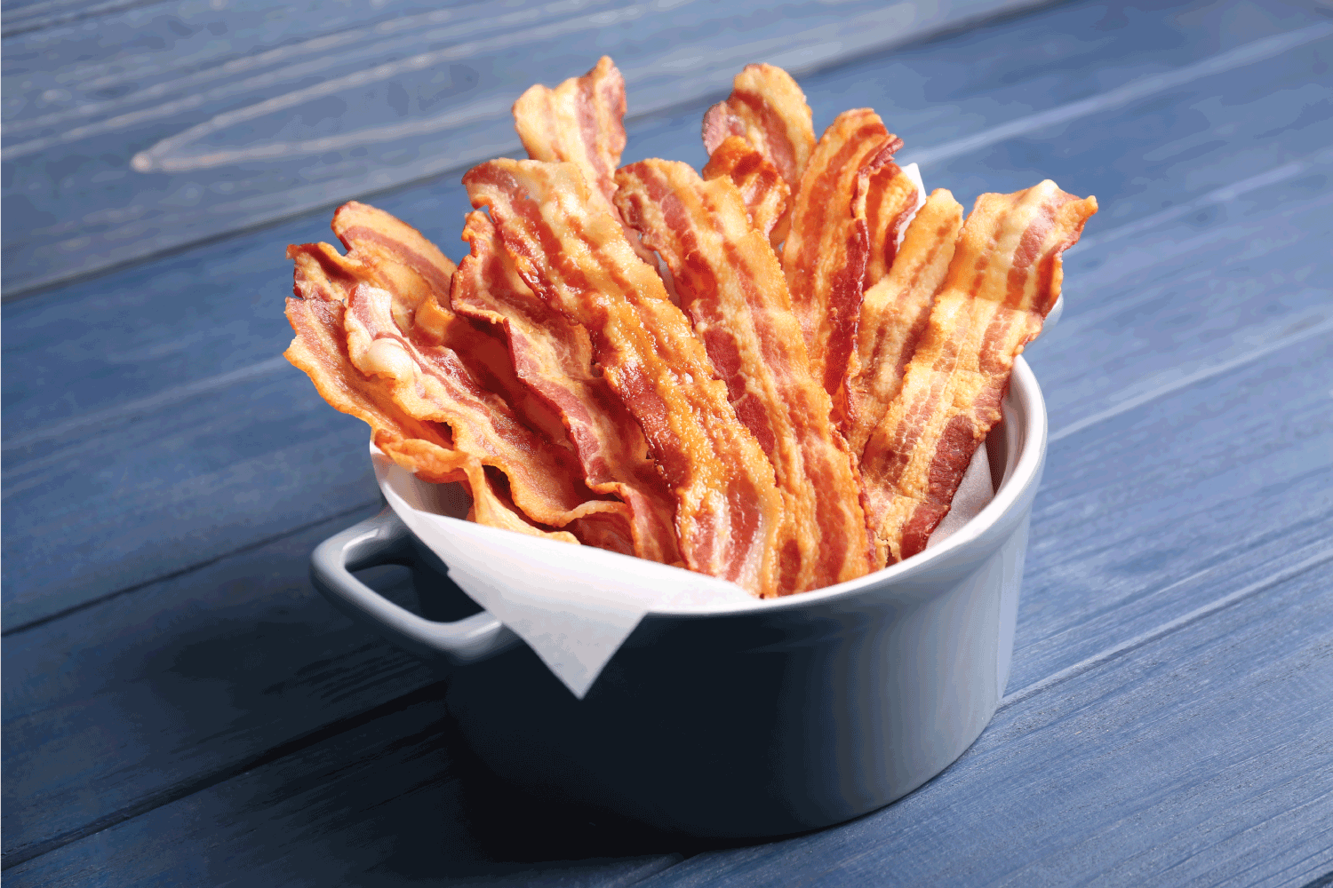 Tasty bacon slices in a ceramic bowl with handles lined with paper towel