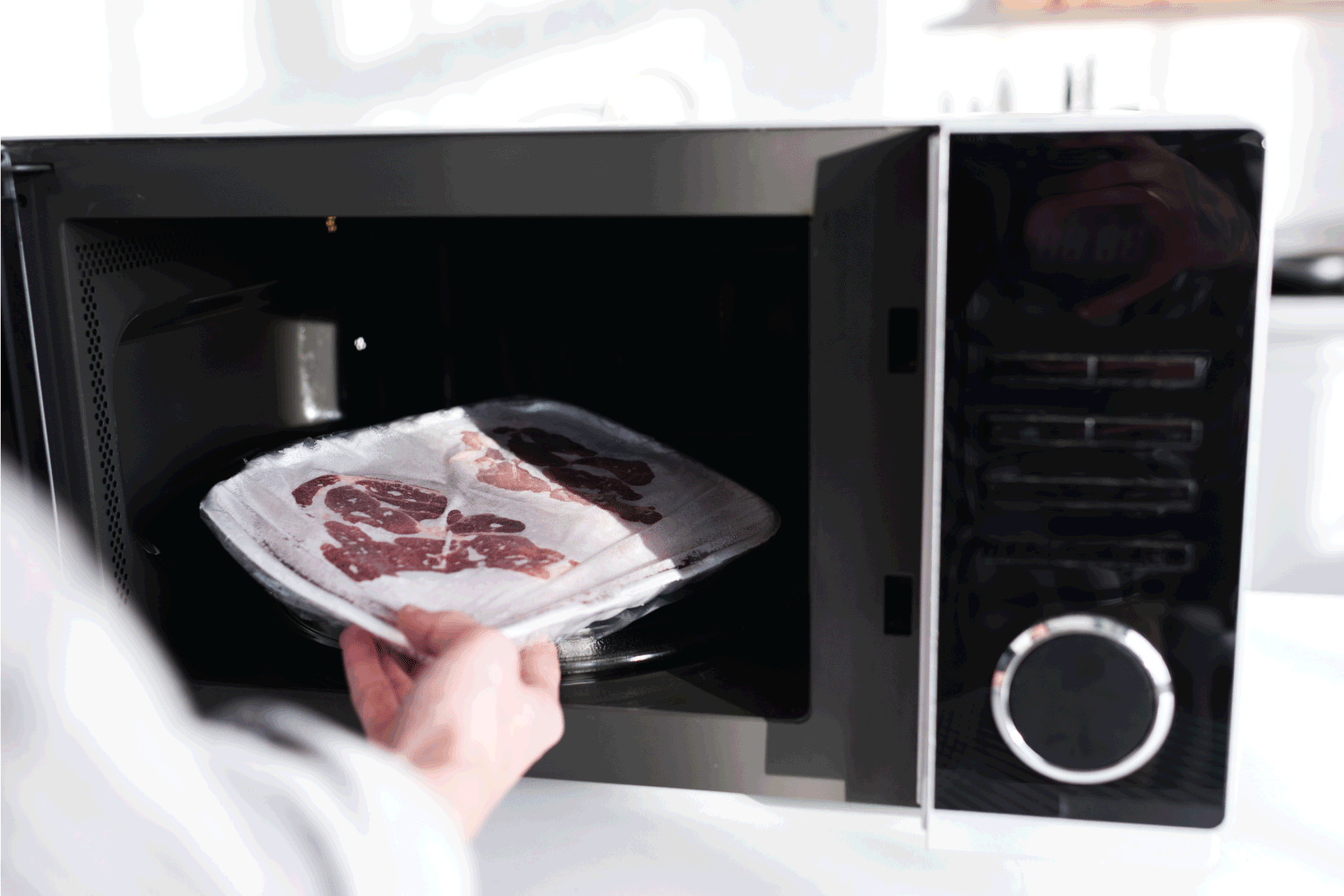 woman putting meat into microwave in kitchen