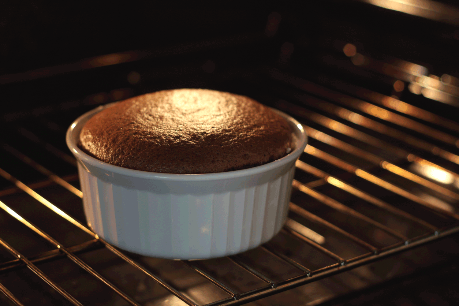 A chocolate soufle baking in a white ramekin