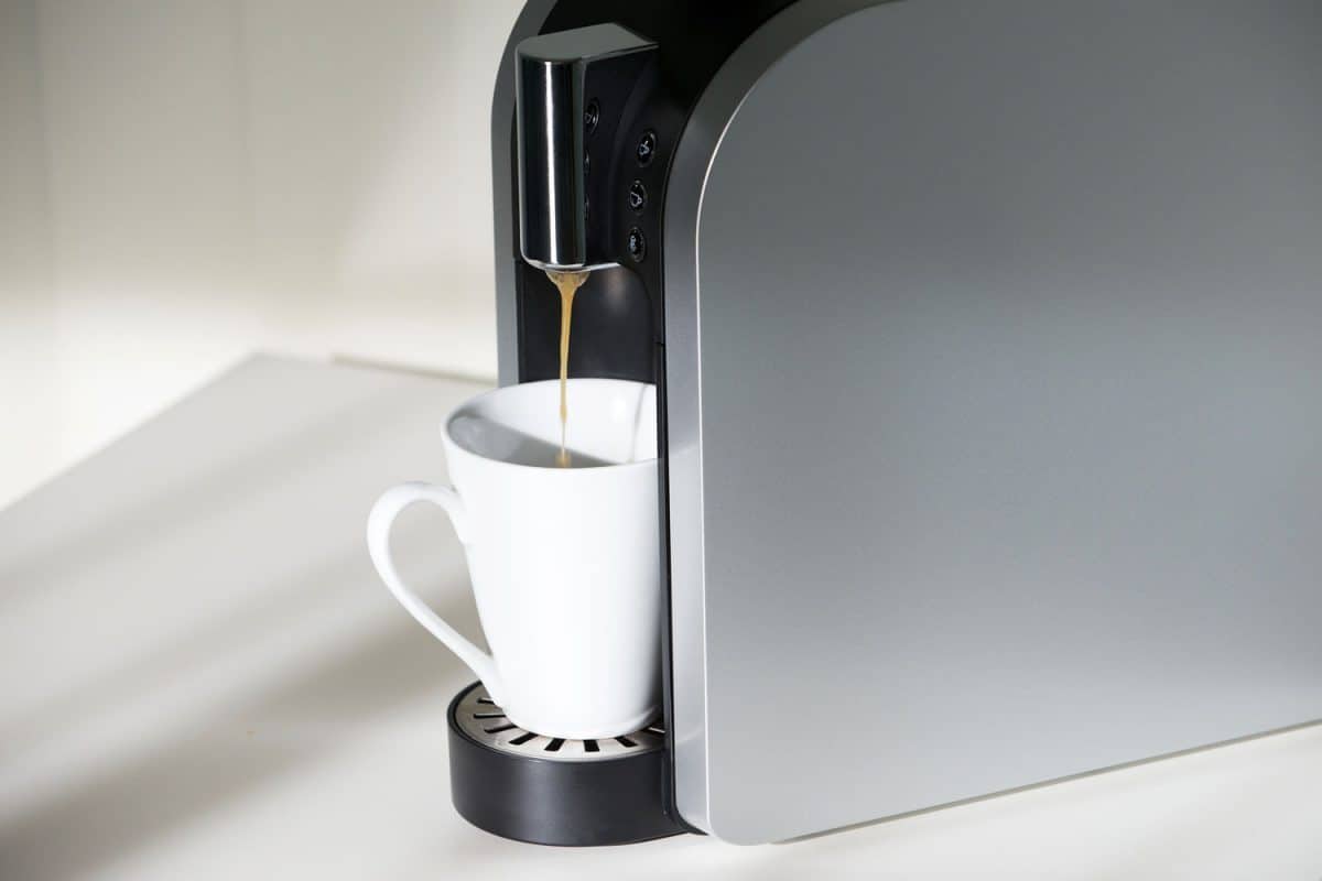 A large coffee maker pouring coffee on a white mug