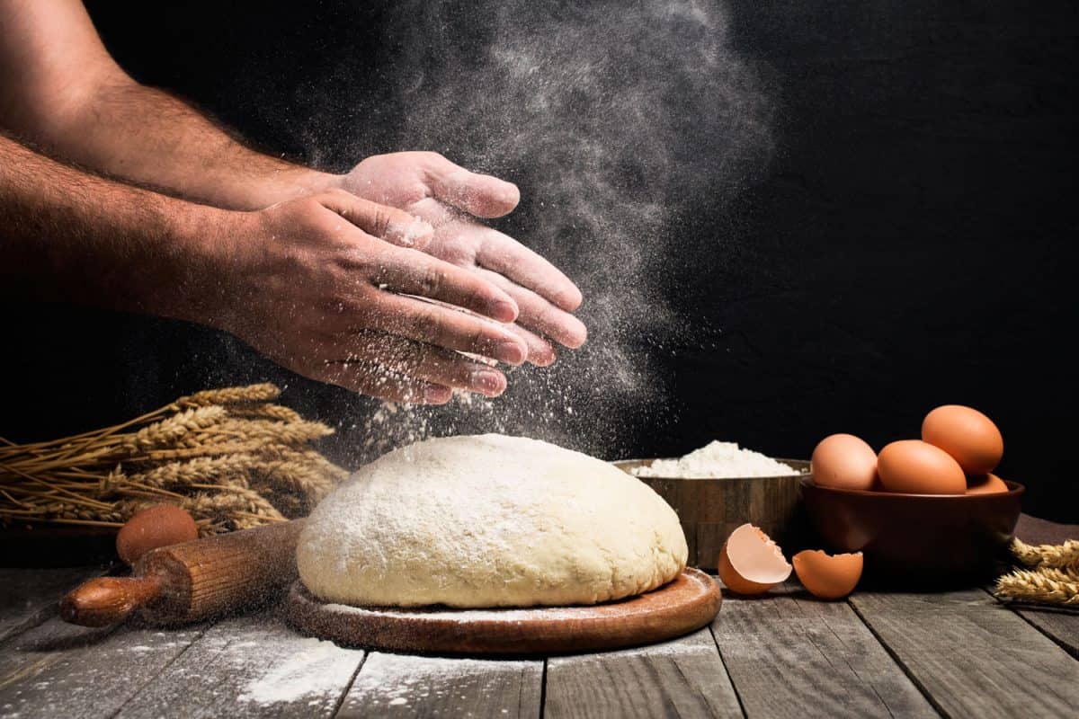 A man slapping flour on his hands over the big pile of dough