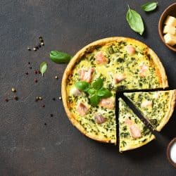A quiche with salmon spinach and cheese placed on top of a concrete table, Do You Have To Defrost Quiche Before Cooking?