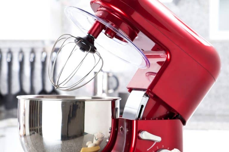 A red electric stand mixer on kitchen counter top with eggs, butter and flour as ingredients for making a pie in the foreground, Can You Fold In With A Kitchenaid Mixer?