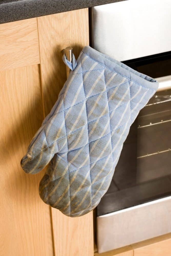 A slightly built oven mitt hanged on the side of the oven