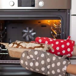 A woman wearing oven mitts removing fresh oven baked bread, Do Oven Mitts Wear Out? [Everything You Need To Know!]