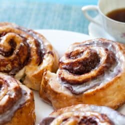 An up close photo of cinnamon rolls with a cup of coffee on the back, How To Keep Cinnamon Rolls Moist