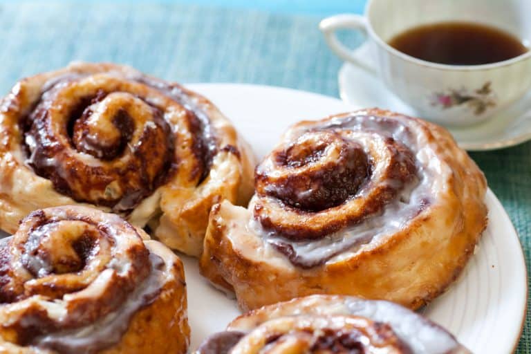An up close photo of cinnamon rolls with a cup of coffee on the back, How To Keep Cinnamon Rolls Moist