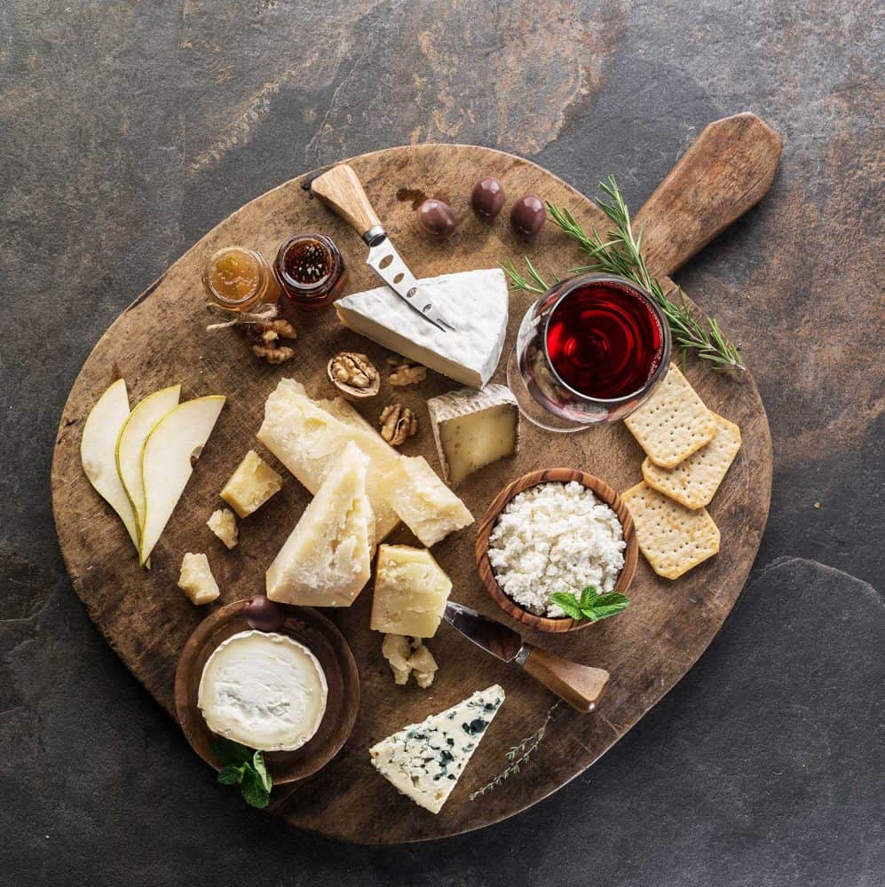 Cheese platter with different cheeses, fruits, nuts and wine on stone background