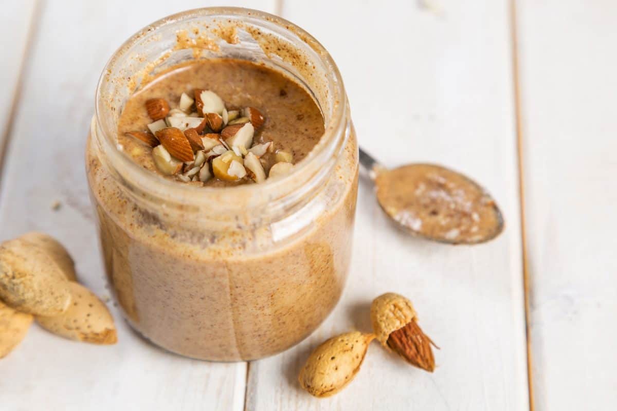 Crushed almond nuts poured inside the jar of almond butter